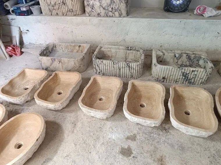A row of rough-cut travertine sinks drying in the workshop yard